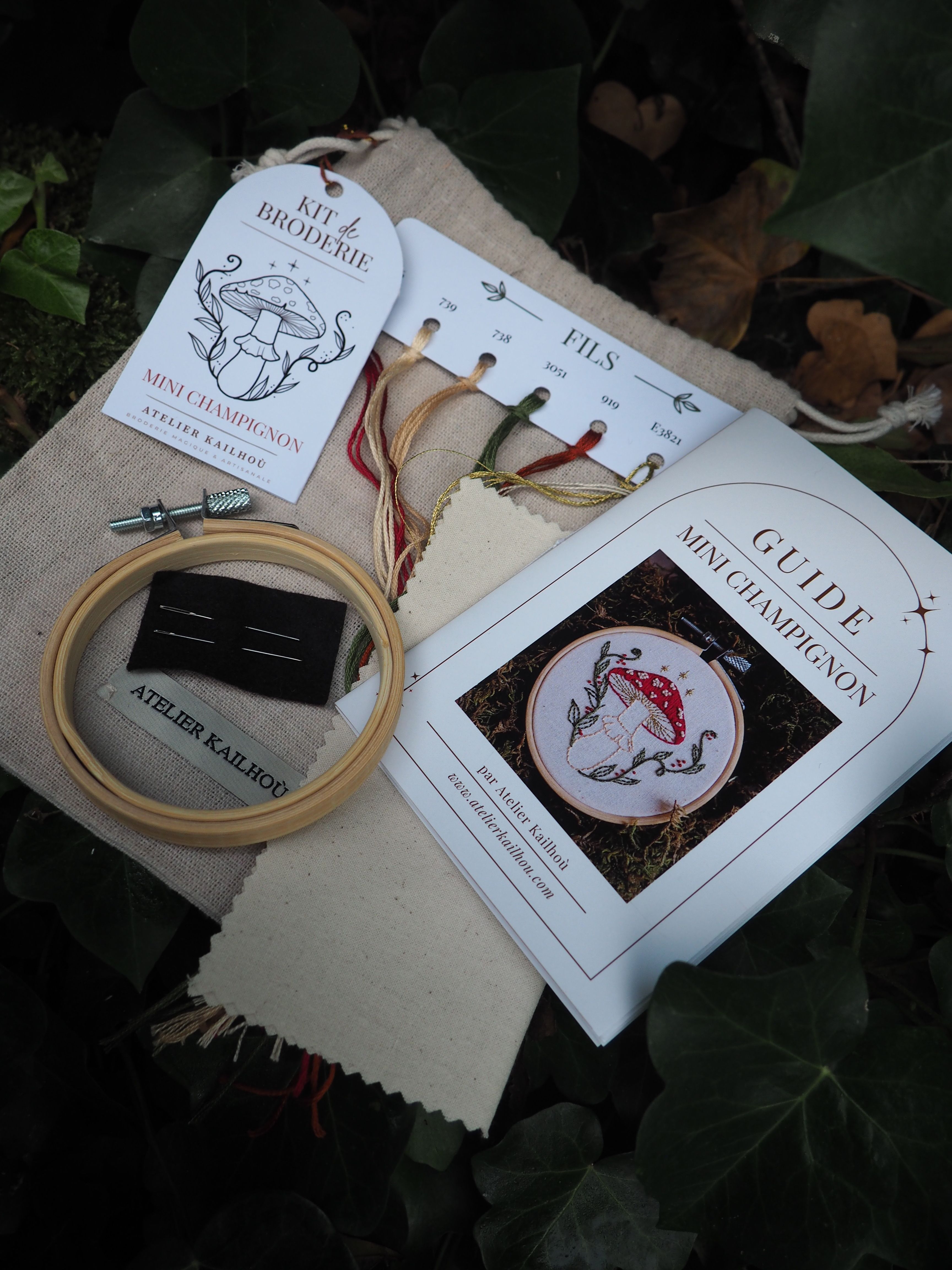 Cette image présente un kit de broderie soigneusement disposé sur ce qui semble être une surface sombre avec des feuilles en arrière-plan. **Éléments visibles :** - **Instructions de broderie** : Plusieurs feuilles blanches avec des diagrammes et motifs, incluant ce qui ressemble à des dessins de poissons ou créatures marines
- **Cercle à broder** : Un tambour en bois de couleur naturelle, outil essentiel pour maintenir le tissu tendu pendant la broderie
- **Tissu** : Une toile de couleur beige/écrue, probablement en lin ou coton, prête à être brodée
- **Fils colorés** : Des écheveaux de fil à broder dans différentes teintes, notamment des rouges et autres couleurs
- **Packaging** : Une pochette ou emballage en tissu naturel L'ensemble suggère un projet de broderie artisanale, avec tous les matériaux nécessaires organisés de manière méthodique. Le style des motifs semble traditionnel ou inspiré de designs classiques de broderie. L'ambiance générale évoque un loisir créatif raffiné et authentique.