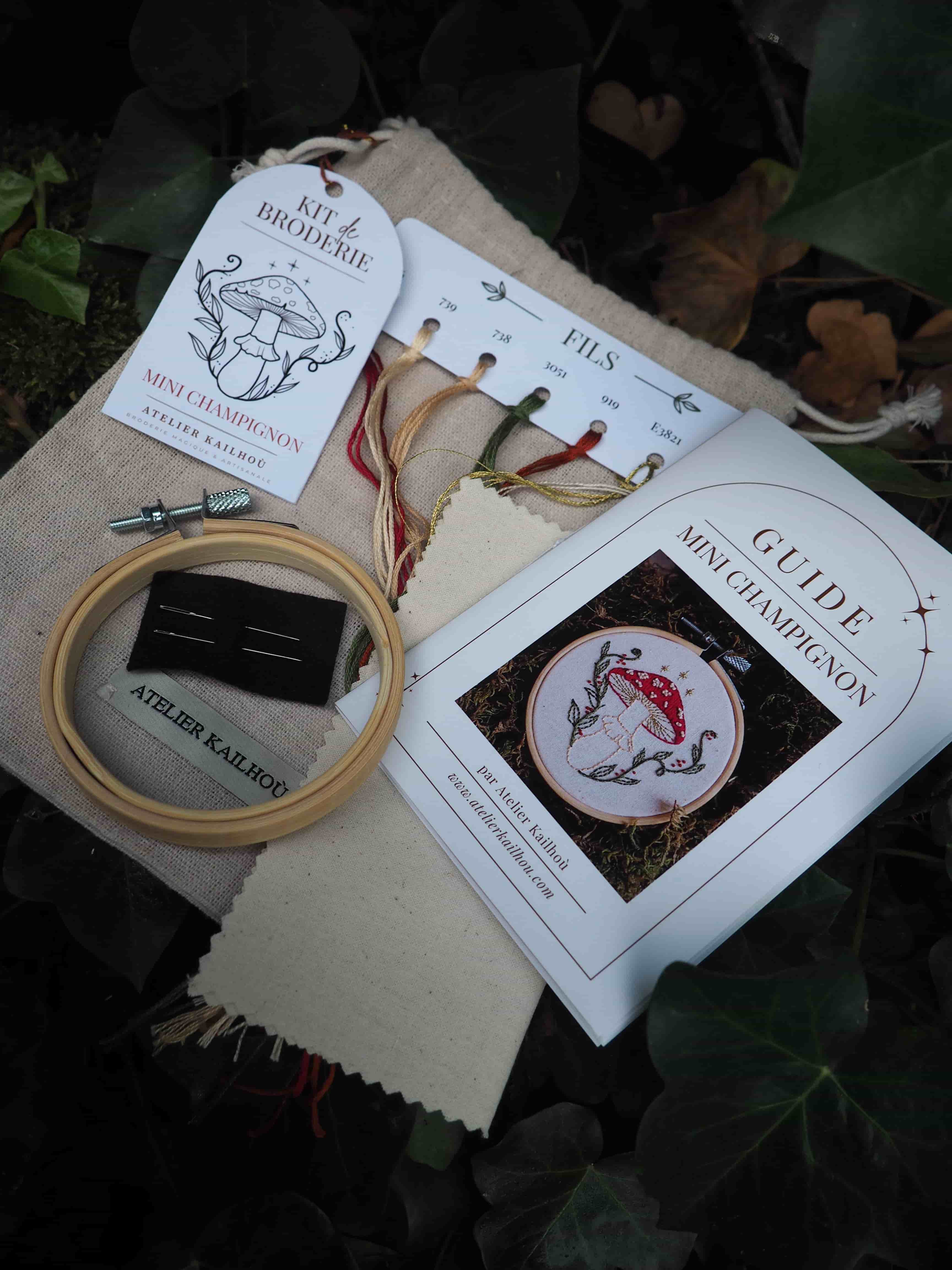 Cette image présente un kit de broderie soigneusement disposé sur ce qui semble être une surface sombre avec des feuilles en arrière-plan. **Éléments visibles :** - **Instructions de broderie** : Plusieurs feuilles blanches avec des diagrammes et motifs, incluant ce qui ressemble à des dessins de poissons ou créatures marines
- **Cercle à broder** : Un tambour en bois de couleur naturelle, outil essentiel pour maintenir le tissu tendu pendant la broderie
- **Tissu** : Une toile de couleur beige/écrue, probablement en lin ou coton, prête à être brodée
- **Fils colorés** : Des écheveaux de fil à broder dans différentes teintes, notamment des rouges et autres couleurs
- **Packaging** : Une pochette ou emballage en tissu naturel L'ensemble suggère un projet de broderie artisanale, avec tous les matériaux nécessaires organisés de manière méthodique. Le style des motifs semble traditionnel ou inspiré de designs classiques de broderie. L'ambiance générale évoque un loisir créatif raffiné et authentique.