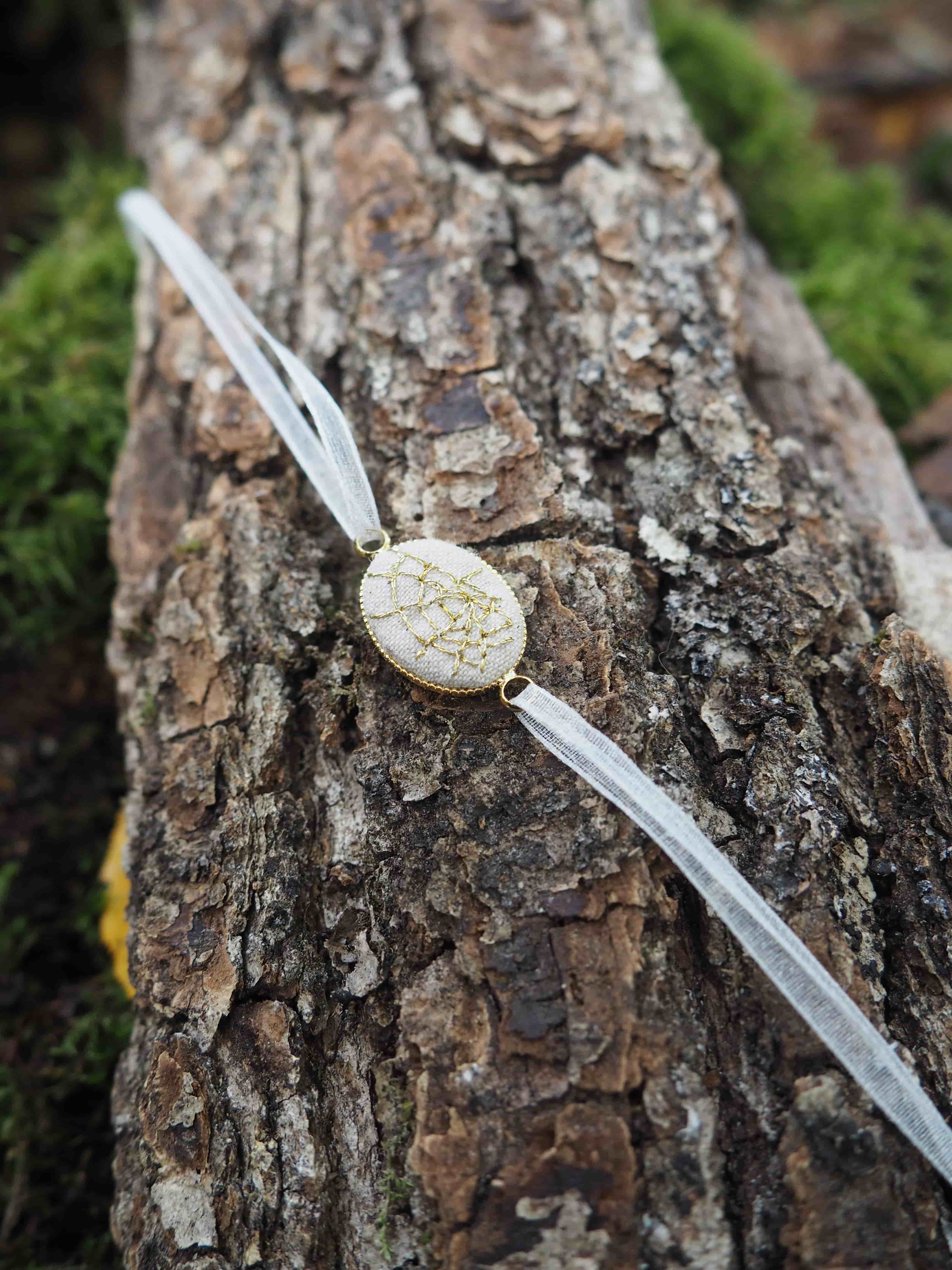 Cette image présente une scène naturelle en gros plan montrant : **L'élément principal :** Une pièce de monnaie dorée ou jaunâtre placée sur l'écorce rugueuse d'un tronc d'arbre ou d'une bûche. La pièce semble être utilisée comme référence d'échelle. **La surface :** L'écorce présente une texture très détaillée avec des motifs naturels, des fissures, des aspérités et une coloration brun-gris caractéristique. On peut observer de petites formations qui pourraient être des lichens ou d'autres micro-organismes. **L'arrière-plan :** Flou artistique (bokeh) montrant de la mousse verte, ce qui suggère un environnement forestier humide et naturel. **L'éclairage :** Naturel et doux, créant une profondeur de champ qui met en valeur la texture de l'écorce tout en gardant l'arrière-plan artistiquement flou. Cette photographie semble avoir été prise dans un contexte scientifique ou naturaliste, la pièce servant probablement d'indicateur d'échelle pour documenter la taille des éléments observés sur l'écorce.