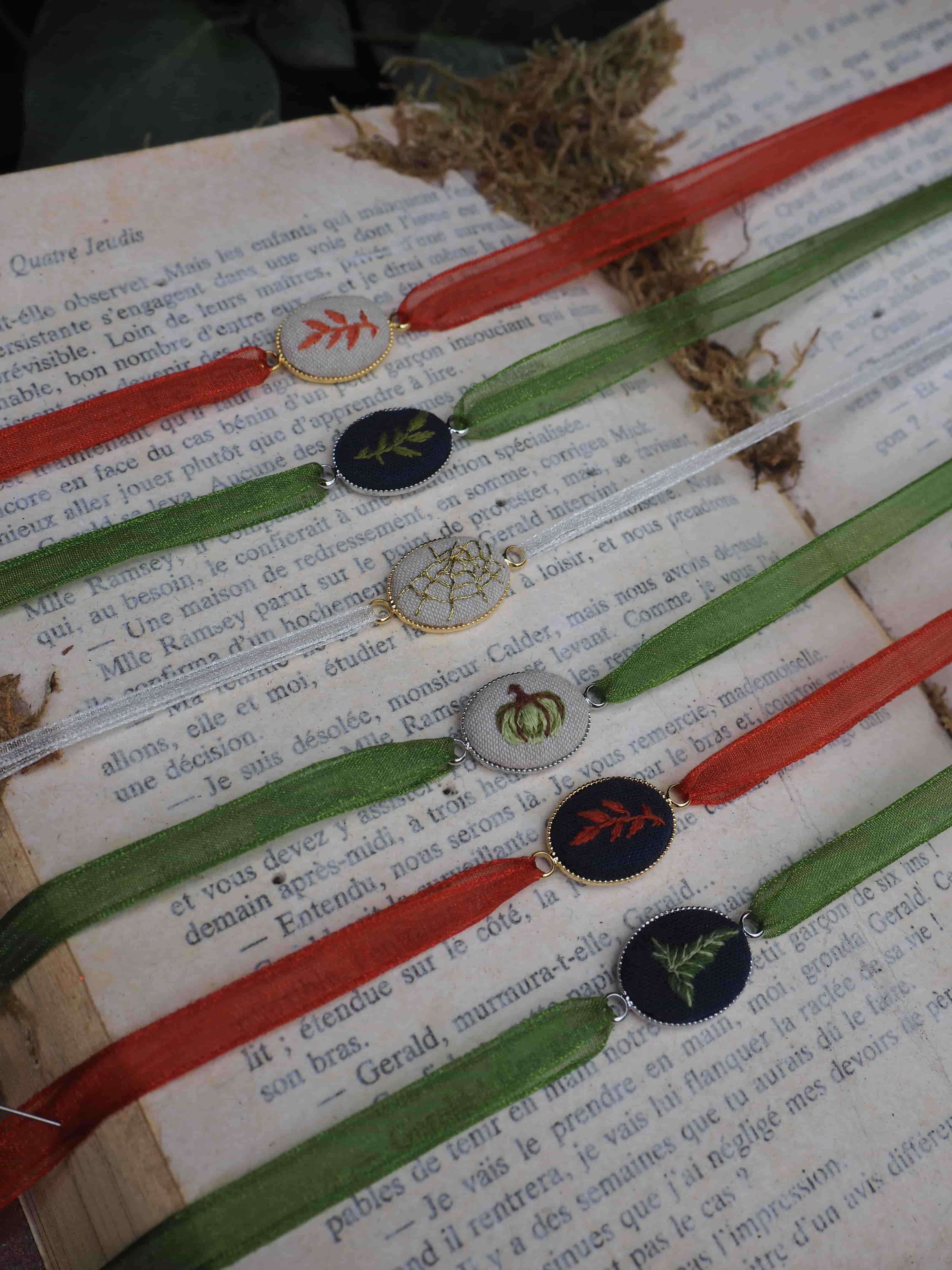 Cette image montre une collection botanique ou un herbier disposé sur des pages de texte. On peut observer : **Les spécimens botaniques :**
- Plusieurs échantillons de plantes séchées et pressées
- Des fragments de mousse ou de lichen de couleur brune/dorée
- Quelques petites fleurs ou graines rondes de couleurs variées (noires, blanches)
- Les spécimens semblent être organisés de manière systématique **La présentation :**
- Les échantillons sont disposés sur des pages de livre ou de documents imprimés
- Des rubans colorés (rouge et vert) traversent horizontalement les pages, créant un motif rayé
- Le texte sous-jacent semble être en français
- L'ensemble donne l'impression d'un travail de classification ou d'étude scientifique **L'aspect général :**
- L'image a une qualité vintage ou artisanale
- La disposition suggère un projet éducatif, artistique ou de recherche en botanique
- Les couleurs sont douces et naturelles, typiques des herbiers traditionnels Cette présentation évoque le travail minutieux des botanistes ou des naturalistes qui collectent, préservent et étudient les spécimens végétaux.